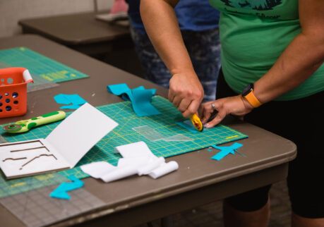 a person in a green shirt using a rotary cutter on fabric.