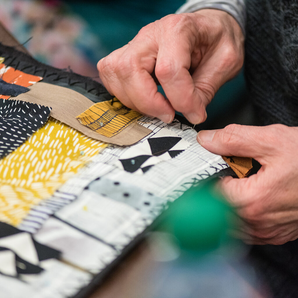 close up of hands with a sewing needle working on a quilt