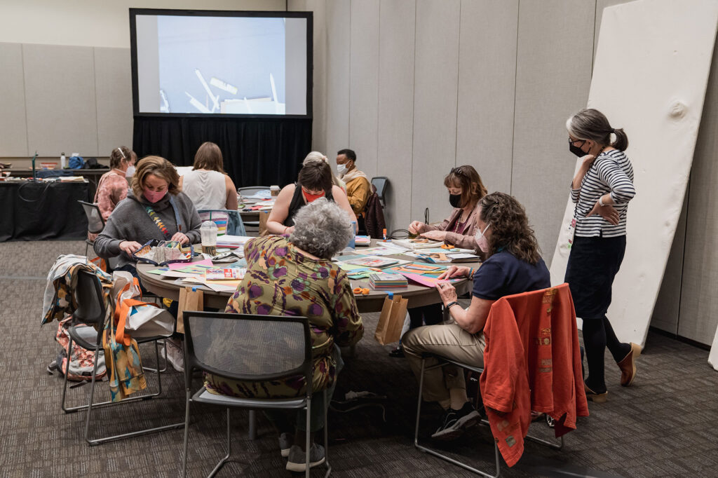 A group of people learns around a table from a quilting teacher
